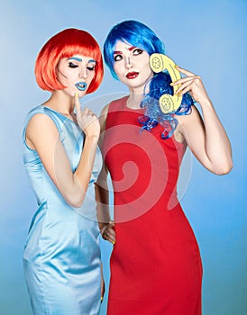 Portrait of young women in comic pop art make-up style. Females in red and blue wigs call on the phone