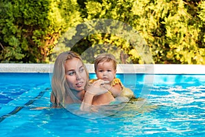 Portrait of young woman instructor swimming in the pool with her little girl