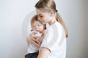 Portrait of young woman mother kissing baby girl daughter on hands at home