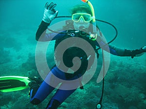 The portrait of young women scuba diver under water. She is in full scuba diving equipment: mask, regulator, BCD. She is showing O