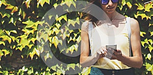 Portrait young women in sunglasses using smart phone isolated on background green nature wall mock up, pretty hipster female hands