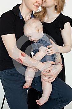 Portrait of young wonderful family in dark clothes with plump cherubic baby infant toddler sitting on white background.