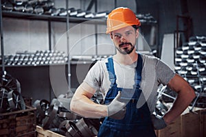 Portrait of a young worker in a hard hat at a large metalworking plant. Shiftman on the warehouse of finished products