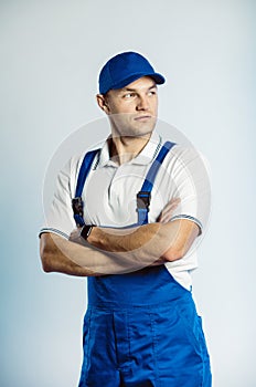 Portrait of young worker man wearing blue uniform with crossing hands. Isolated on grey background with copy space. Human face