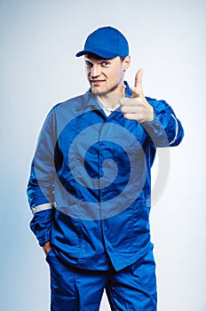 Portrait of young worker man wearing blue uniform. Pointing finger at you looking at camera. Isolated on grey background with copy