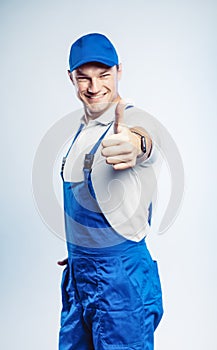 Portrait of young worker man wearing blue uniform. Showing thumb up. Movement cool. Isolated on grey background with copy space.