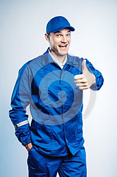 Portrait of young worker man wearing blue uniform. Showing thumb up. Movement cool. Isolated on grey background with copy space.