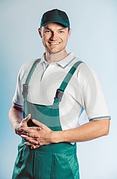 Portrait of young worker man wearing green uniform with crossing hands. Isolated on grey background with copy space. Human face