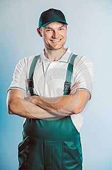 Portrait of young worker man wearing green uniform with crossing hands. Isolated on grey background with copy space. Human face