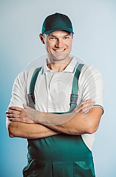 Portrait of young worker man wearing green uniform with crossing hands. Isolated on grey background with copy space. Human face