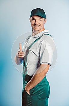 Portrait of young worker man wearing green uniform. Pointing finger at you looking at camera. Isolated on grey background with