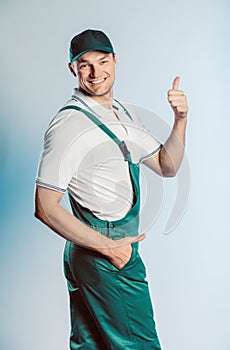 Portrait of young worker man wearing green uniform. Showing thumb up. Movement cool. Isolated on grey background with copy space.