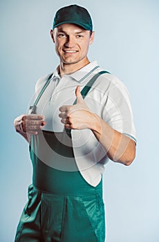 Portrait of young worker man wearing green uniform. Showing thumb up. Movement cool. Isolated on grey background with copy space.