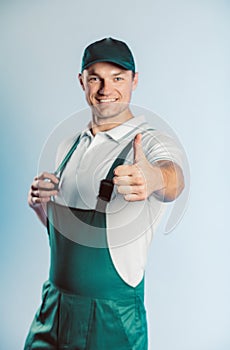 Portrait of young worker man wearing green uniform. Showing thumb up. Movement cool. Isolated on grey background with copy space.