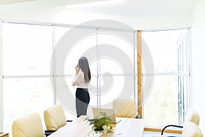 Portrait of young worker speaking using cell phone, looking out the window. Female having business call, busy at her workplace.
