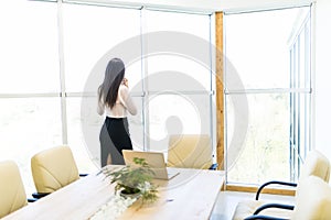 Portrait of young worker speaking using cell phone, looking out the window. Female having business call, busy at her workplace.