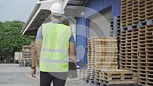 Portrait of young worker working in logistic industry outdoor in front of factory warehouse. Man with hard hat looking