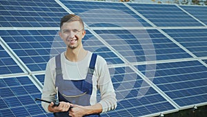 Portrait of a young worker in workwear, smiling and looking at the camera. Against the background of solar panels