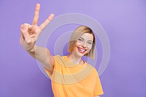 Portrait of youngster girl showing v sign gesture straight on camera say hi greet friends isolated purple color