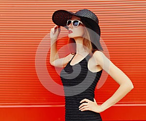 Portraitbeautiful young woman wearing a black summer hat and dress on red background