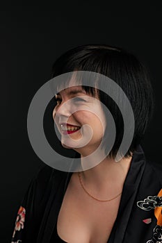 Portraite of beautiful smiling woman. girl looking aside. black short haircut, red lipstick on a dark background in the studio.