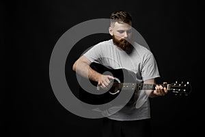 Portraite of handsome brunette bearded man musician, guitarist standing and holding a acoustic guitar in a hand.