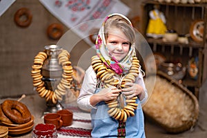 Portraite of little girl in a traditional Russian headscarf and sundress with bunch of bagels.
