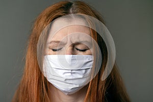 Portraite of a young red-haired woman wearing respiratory medical mask clothing her eyes.