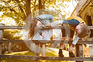 Portraits of happy kids boy and girl on wooden fence. Children playing upside down outdoors in summer park. Kids happy
