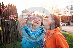 Portraits of a smiling grandmother and granddaughter sniffing a branch of lilac. Springtime