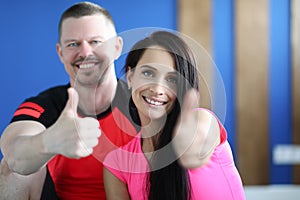 Portraits of smiling man and woman in gym and showing thumbs up gesture