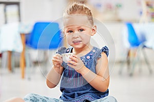 Portrat of one adorable little caucasian girl sitting alone in preschool and holding a small teacup. Smiling child photo