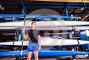 Portrat of young canoeist standing in front of stacked canoes. Concept of canoeing as dynamic and adventurous sport. photo