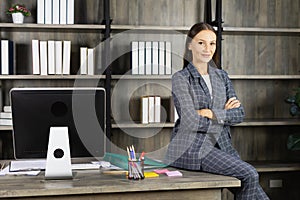 portrati of young woman cross arm, sit on table, and looks at camera with copy space in workplace. beautiful young woman look as