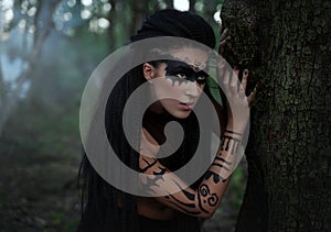 Portret close up of beautiful tribal shaman woman in a foggy forest.Amazon girl near the tree. Soft focus