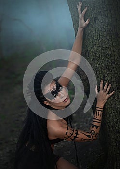 Portret close up of beautiful tribal shaman woman in a foggy forest. Hands of ethnic dancer.Amazon girl near the tree. Soft focus