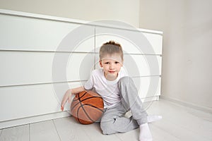 Portret of a little smiling schoolboy looking at camera sitting on the floor at his white room