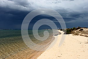 Portugal. Algarve. Ilha deserta. Sand and ocean before storm on dark blue sky background, horizontal view. photo