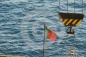 Portugal flag flapping on black mast situated in aft or stern part of container ship.