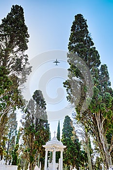 Portugal Travel Concepts. Airplane Flying Over the Old Graveyard with Gazibo with Cross Along Green Pines in Lisbon