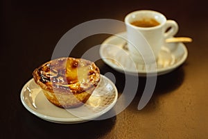 Portuguese summer breakfast. Pastel de nata and small coffee. Sweet egg custard tart pastry on black table.