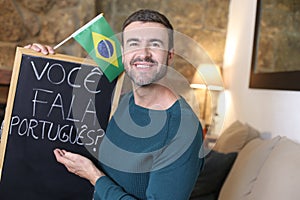 Portuguese teacher holding blackboard and Brazilian flag. TRANSLATION OF THE TEXT IN THE IMAGE: `Do you speak Portuguese?`