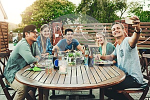 Pose for the gram guys. a group of young friends posing together around a table while taking a selfie outdoors.