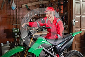 Pose of young mechanic in wearpack uniform and hat standing beside a dirt bike