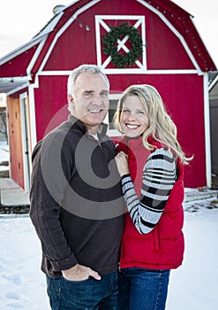 Posed portrait of a attractive mature couple outdoors by a red barn during the Christmas season. Happy Holidays