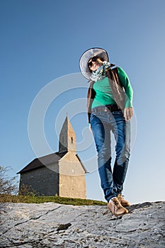 Posing young woman in a stylish hat and an old romanesque church