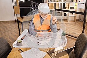 Positiv bearded mature man wearing orange reflective vest, and construction hard hat.