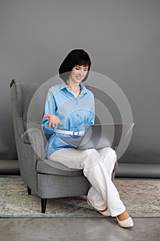 Positive adult business woman mentor teacher psychologist sits on armchair consulates talk in online seminar on laptop