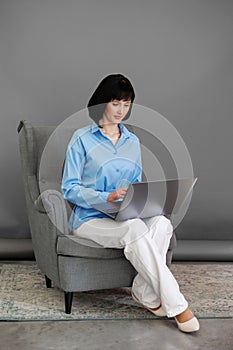 Positive adult business woman mentor teacher psychologist sits on armchair consulates talk in online seminar on laptop