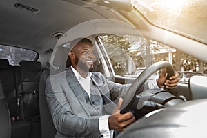 Positive african american businessman driving car, sun flare